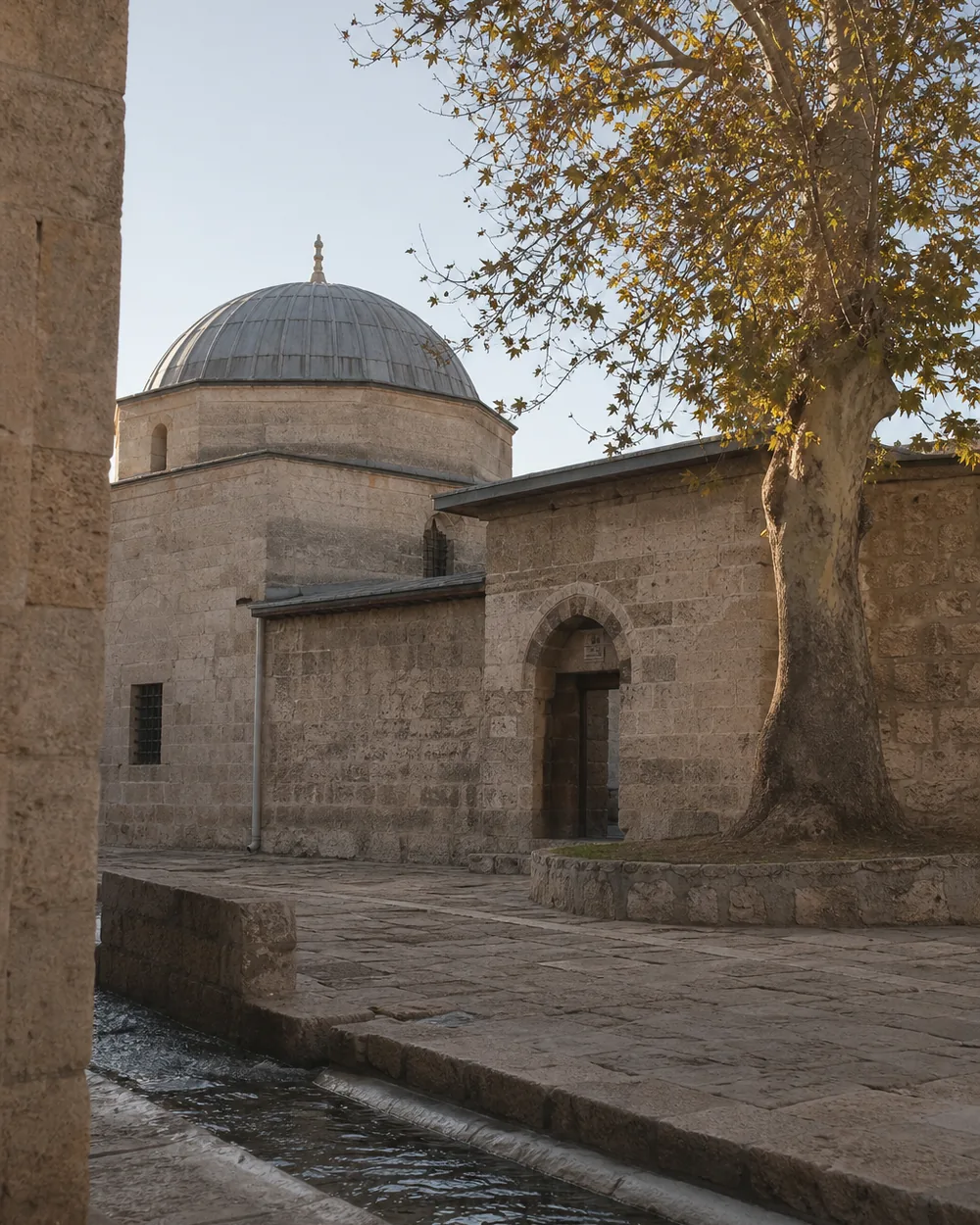 Taş avlu, kurşun kaplı kubbe, kemerli kapı, avluda bir çınar ve taş su kanalı