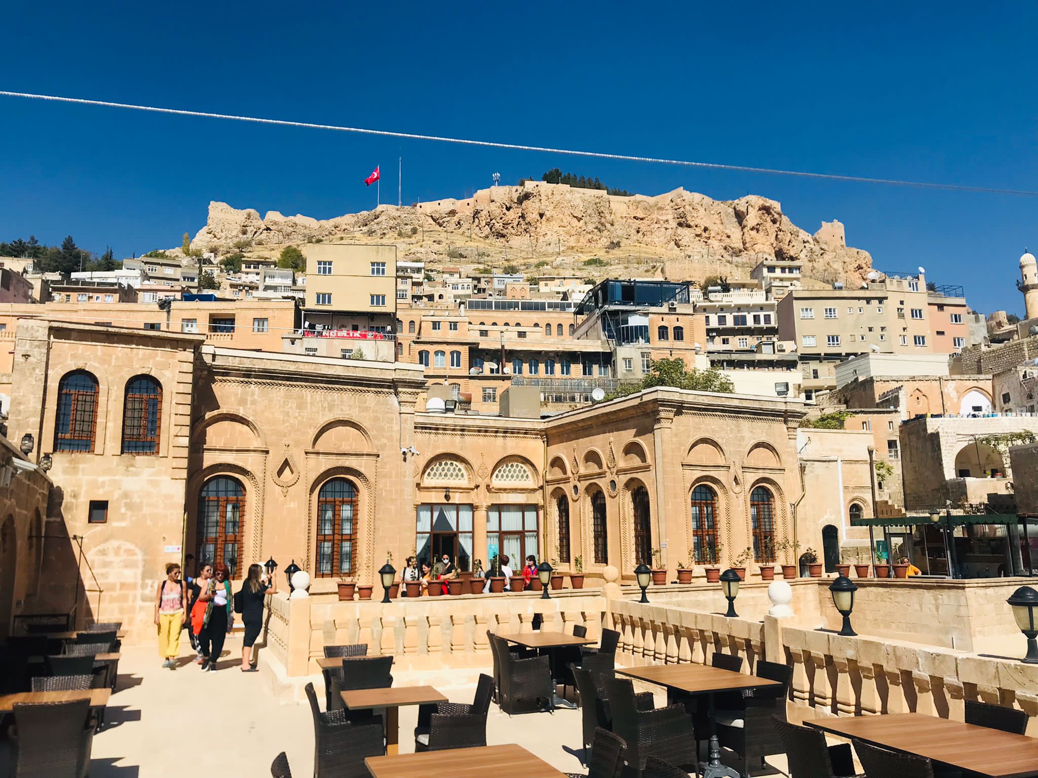 Taş yapıların önündeki teras ve arkada Mardin Kalesi